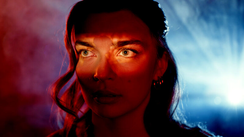 Portret van een vrouw met accentverlichting, in schakeringen van rood en blauw, met een intense blik.