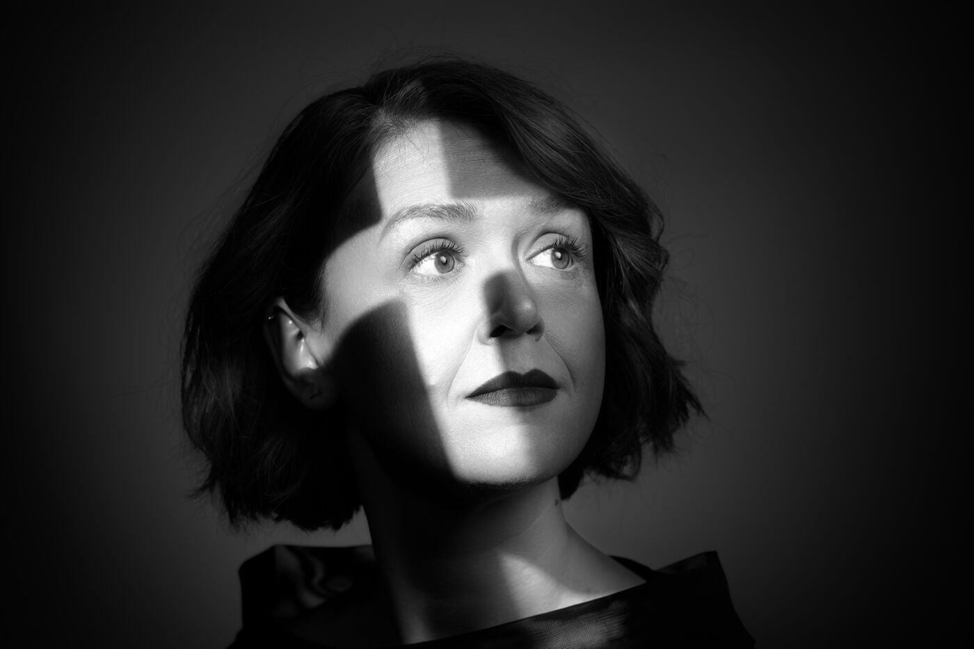 Portret in zwart-wit van een vrouw met kort haar, schaduwen over haar gezicht, met een neutrale uitdrukking.