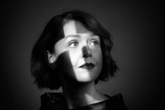 Portret in zwart-wit van een vrouw met kort haar, schaduwen over haar gezicht, met een neutrale uitdrukking.