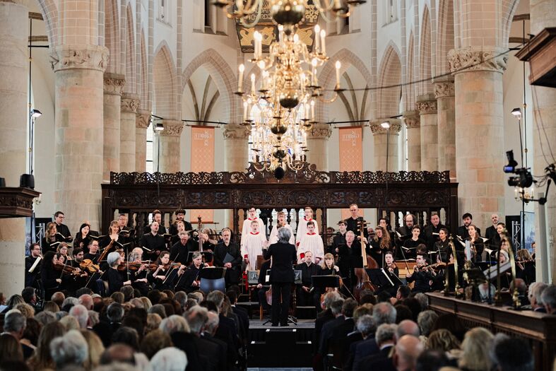 Een orkest en koor optreden in een historische kerk met een publiek dat luisterend aanwezig is.