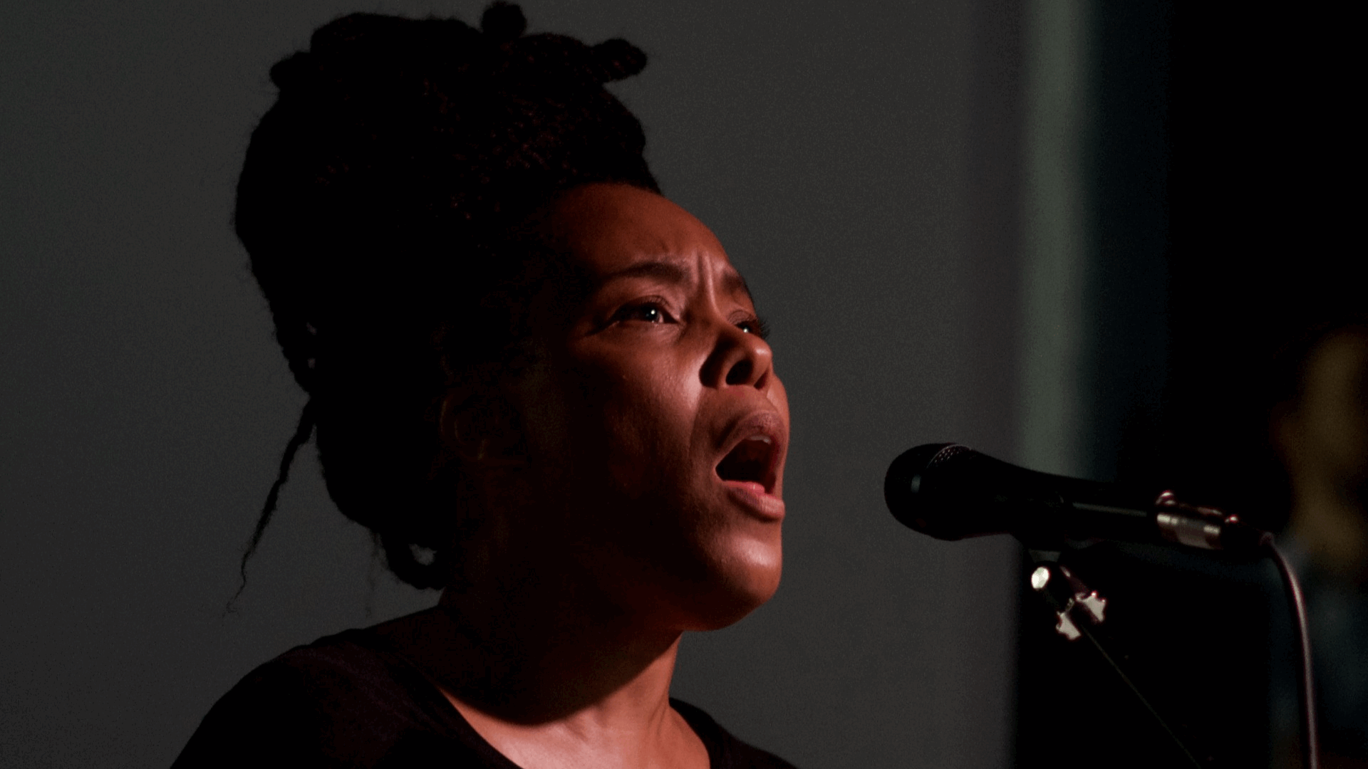 Elaine Mitchener zingt in een microfoon met een intense expressie tijdens een optreden.