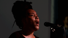Elaine Mitchener zingt in een microfoon met een intense expressie tijdens een optreden.