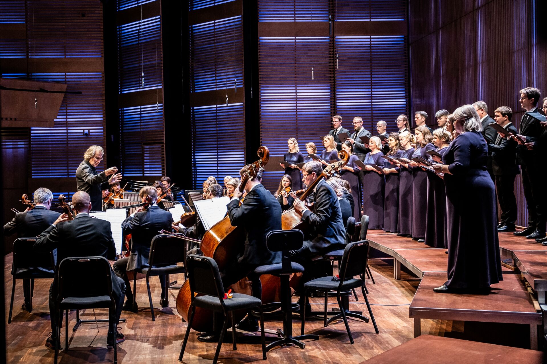 Orkest en koor voeren een muzikale voorstelling uit op een podium met warm verlichte achterwand.