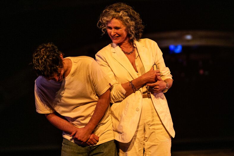 Twee personen op een podium; een man in een casual shirt en een vrouw in een witte outfit, lachend met een speelse interactie.