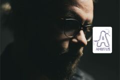 Portret van een man met een baard, bril en donker haar in een licht gespote omgeving, met een contemplatieve uitstraling.