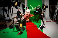 Filmset met groene achtergrond, rode loper, meerdere personen, camera‑lampen en rekwisieten.