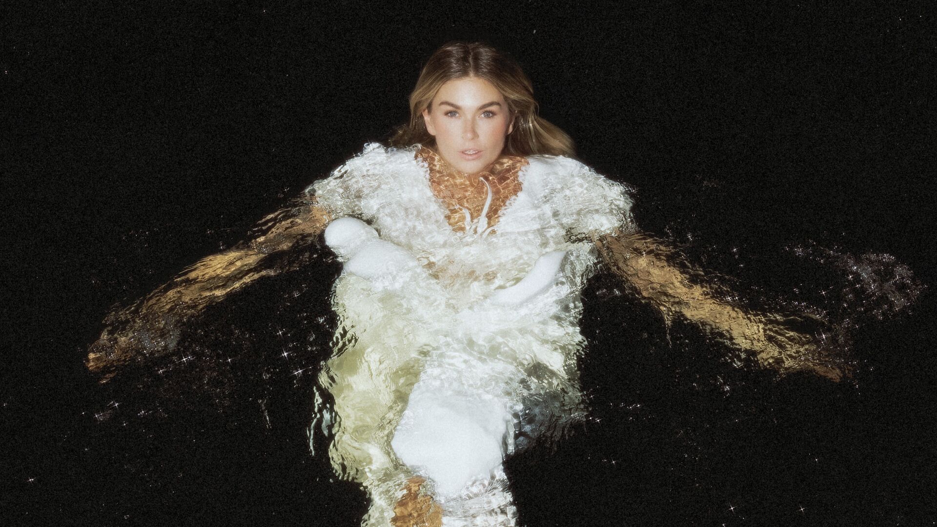 Roxanne Hazes in water in een witte jurk met een donkere achtergrond.