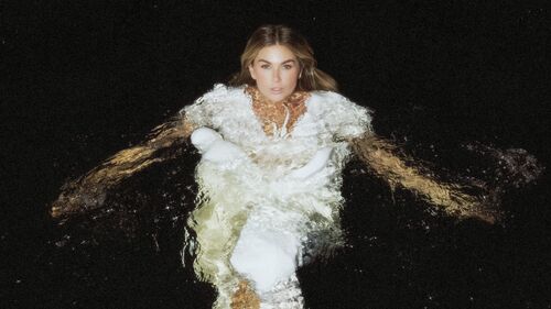 Roxanne Hazes in water in een witte jurk met een donkere achtergrond.