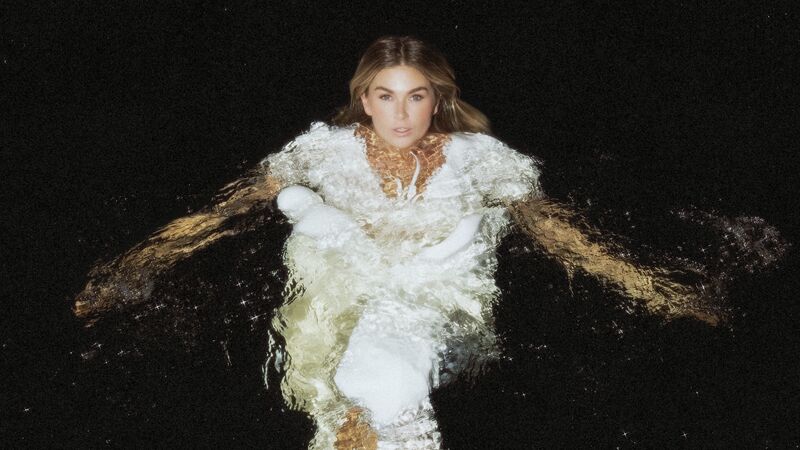 Roxanne Hazes in water in een witte jurk met een donkere achtergrond.