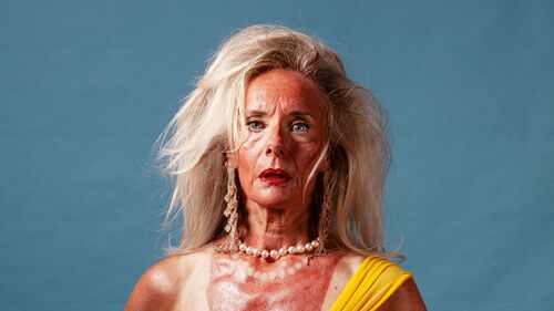 Een vrouw in een gele badoutfit met een bezorgde uitstraling, poseert tegen een blauwe achtergrond.