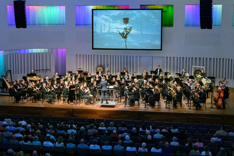 Groot orkest speelt op podium met dirigent vooraan en publiek in de zaal.