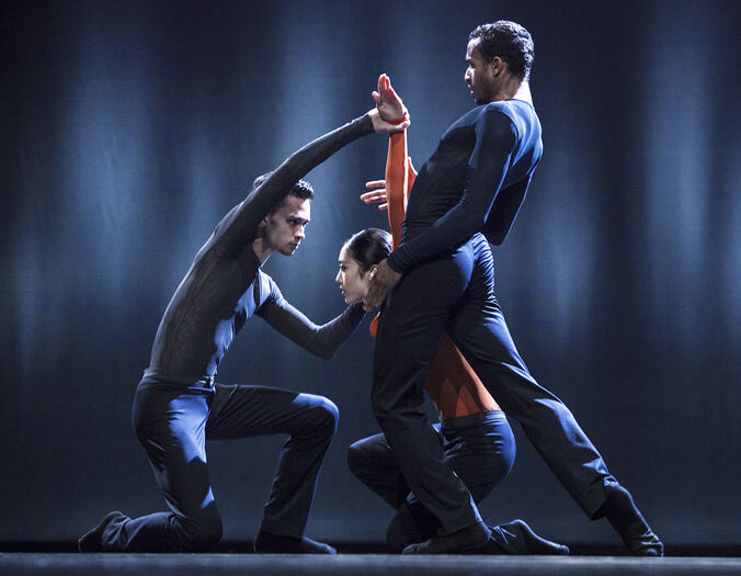 Drie dansers in een dynamische pose, met een focus op beweging en samenwerking op een donkere achtergrond.