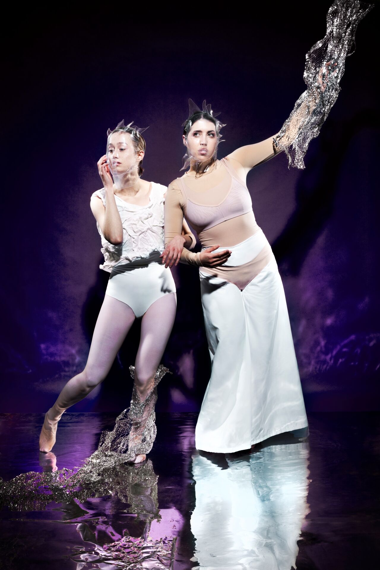 Twee performers in artistieke outfits poseren tegen een paarse achtergrond, met dramatische poses en expressieve gezichten.