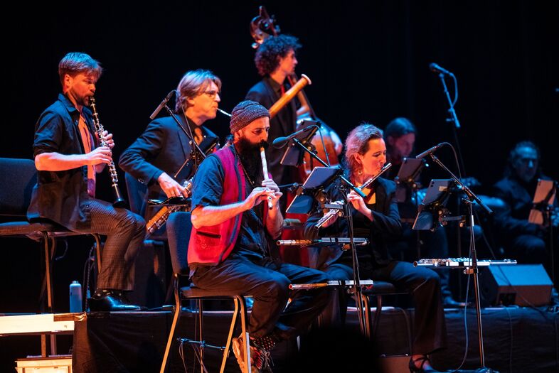 Groep muzikanten speelt samen op een podium met verschillende instrumenten tijdens een live optreden.