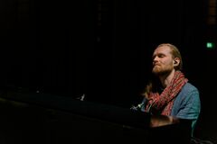 Man met een sjaal speelt piano in een donkere ruimte, met een serene uitstraling.