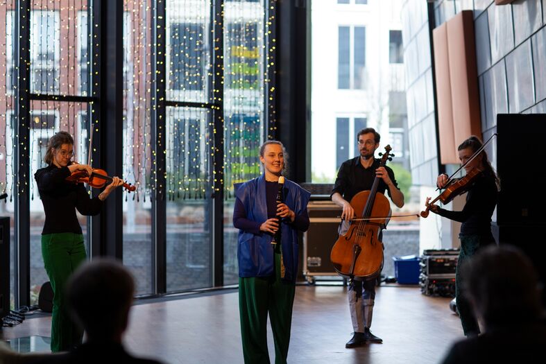 Een muzikant zingt op een podium terwijl twee violisten en een cellist optreden in een moderne ruimte.