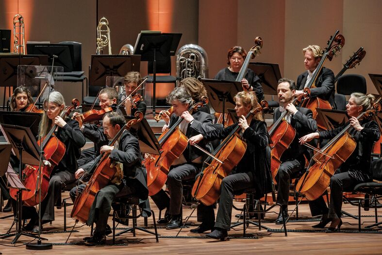 Een orkest met violisten en cellisten speelt op het podium van een concertzaal.