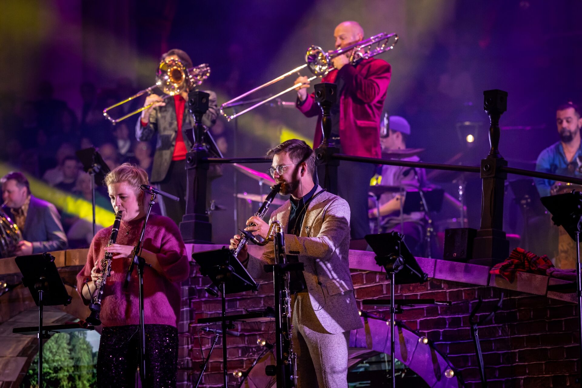 Een live band bestaat uit muzikanten met verschillende instrumenten, uitgevoerd op een kleurrijk verlichte scène.