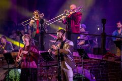 Een live band bestaat uit muzikanten met verschillende instrumenten, uitgevoerd op een kleurrijk verlichte scène.