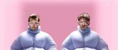 Twee personen in opgeblazen lichtblauwe pakken rennen synchroon naar voren tegen een roze achtergrond.