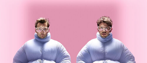 Twee personen in opgeblazen lichtblauwe pakken rennen synchroon naar voren tegen een roze achtergrond.