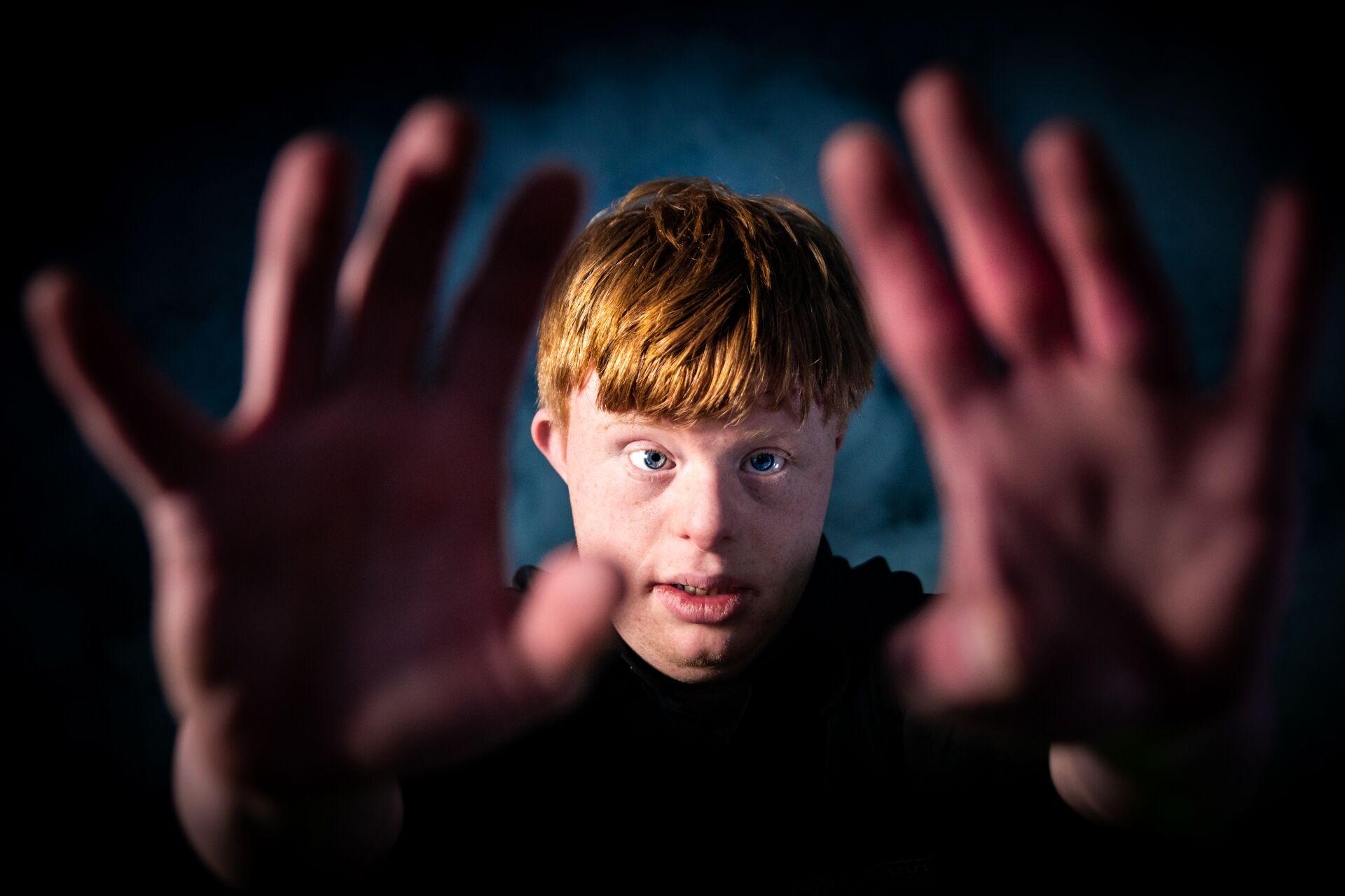 Jonge man met rode haren houdt zijn handen omhoog tegen een donkere achtergrond.