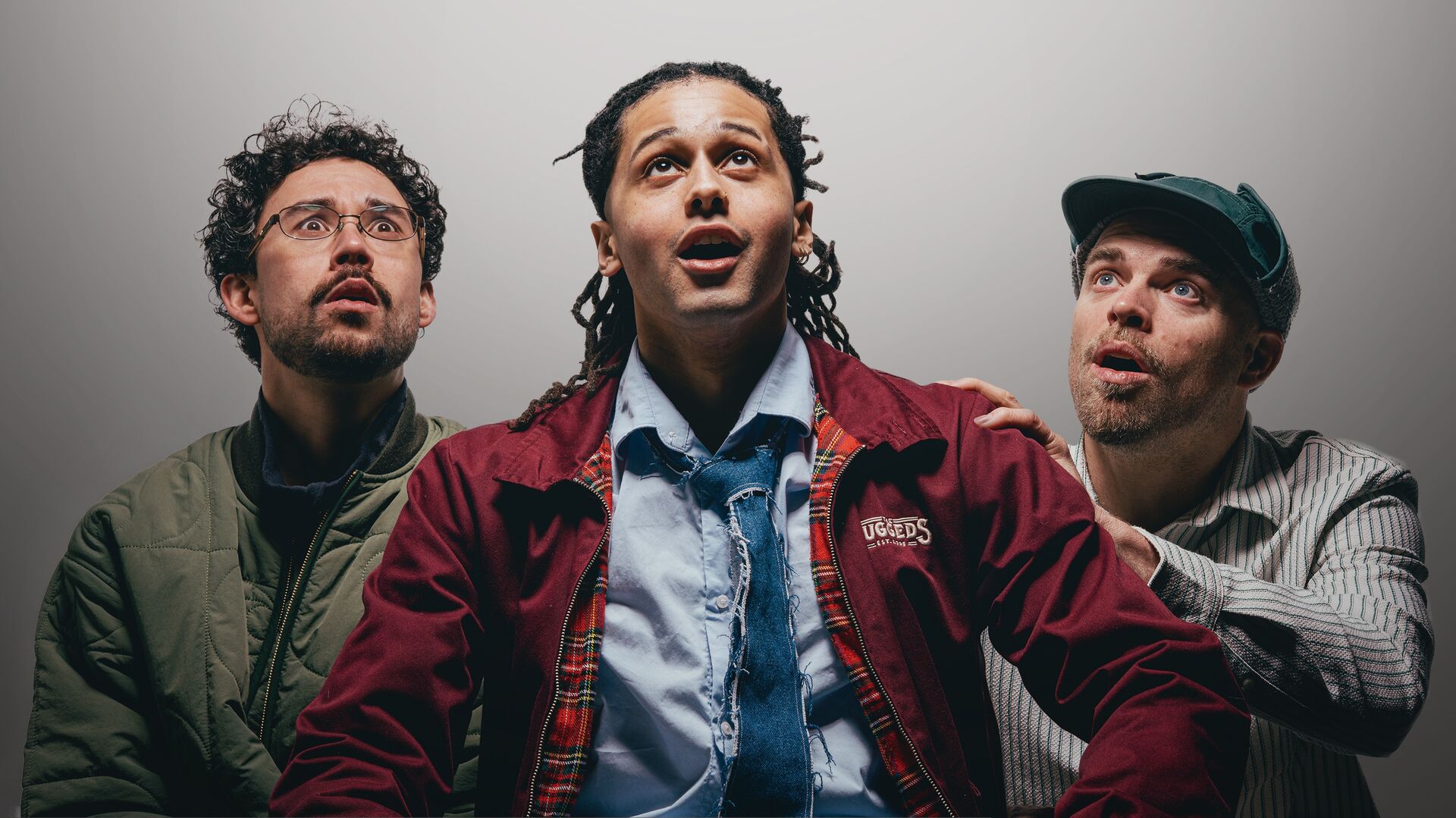 Drie mannen kijken omhoog met verwondering, met een lichte dramatise in hun gezichtsuitdrukkingen en kleding.