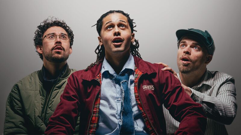 Drie mannen kijken omhoog met verwondering, met een lichte dramatise in hun gezichtsuitdrukkingen en kleding.
