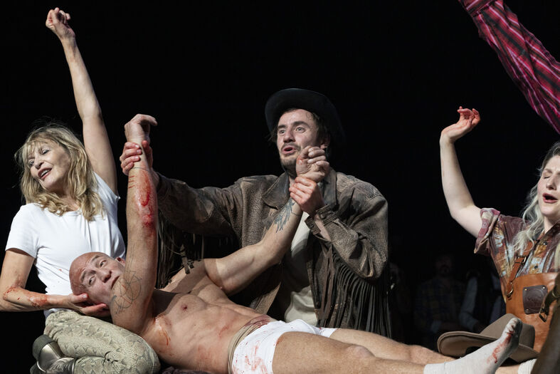 Theateruitvoering met acteurs in uitgebreide kostuums, enkele mensen hebben bloed op hun handen.
