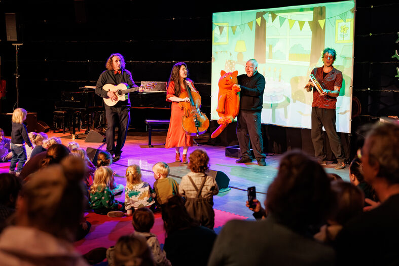 Een optreden met muzikanten en een poppenkastshow voor kinderen, met een kleurrijke setting en een betrokken publiek.