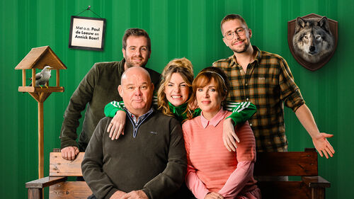 Vijf personen poseren voor een felgroene wand, zittend en staand rond een houten bank.