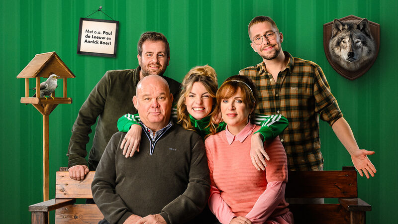 Vijf personen poseren voor een felgroene wand, zittend en staand rond een houten bank.