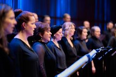 Koorleden in zwarte kleding zingen op een podium met blauwe verlichting.