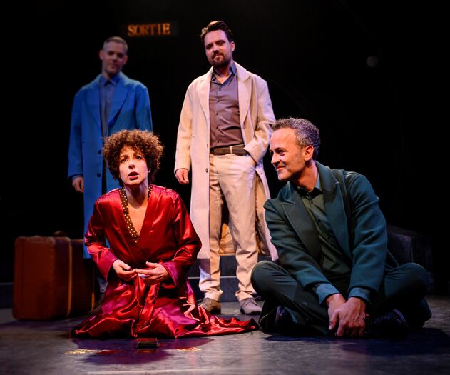 Vier acteurs op een theaterpodium, gekleed in kleurrijke kostuums, in een intense scènesamenstelling.