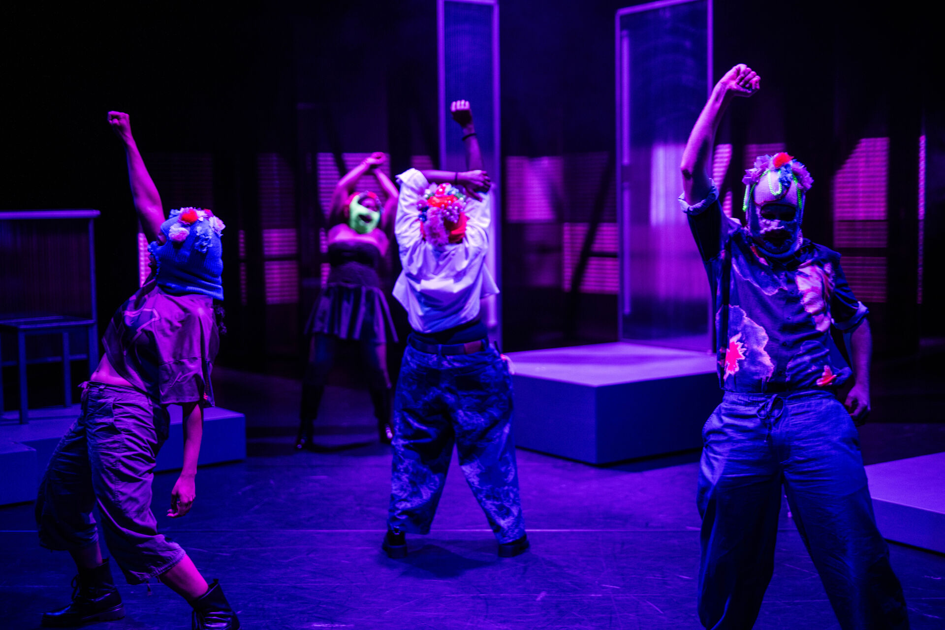 Groep performers met kleurrijke maskers voert een dansuitvoering op een podium met paarse verlichting.