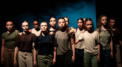 Groep van tien dansers in een donkere ruimte, met intense gezichten en een blauwe achtergrond, allen in casual kleding.
