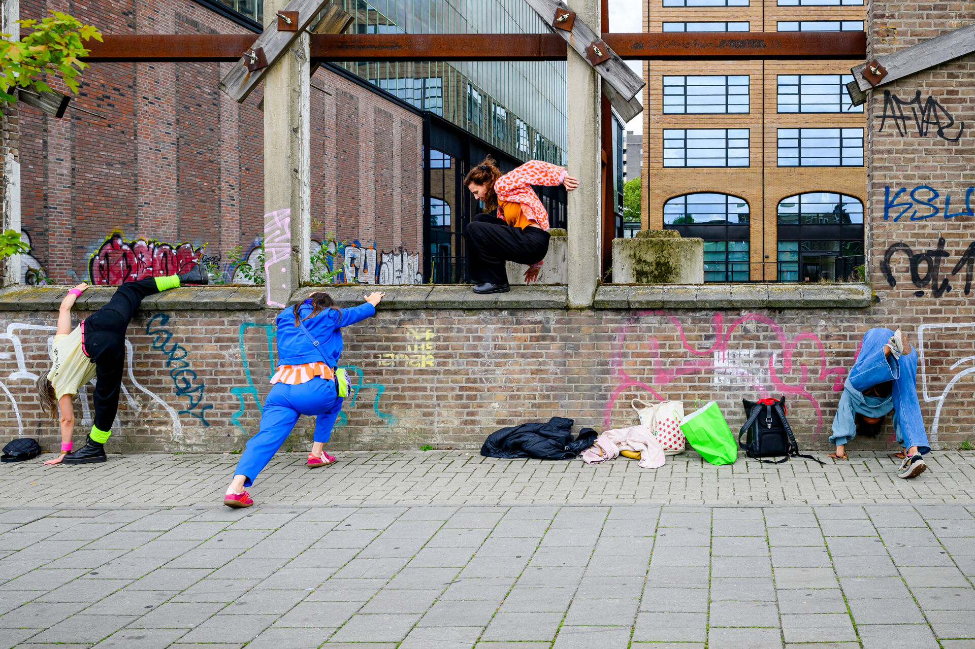 Groep jongeren aan het oefenen met parkour, waarbij ze over een muur klimmen en zich aanpassen aan hun omgeving.