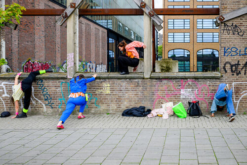 Groep jongeren aan het oefenen met parkour, waarbij ze over een muur klimmen en zich aanpassen aan hun omgeving.