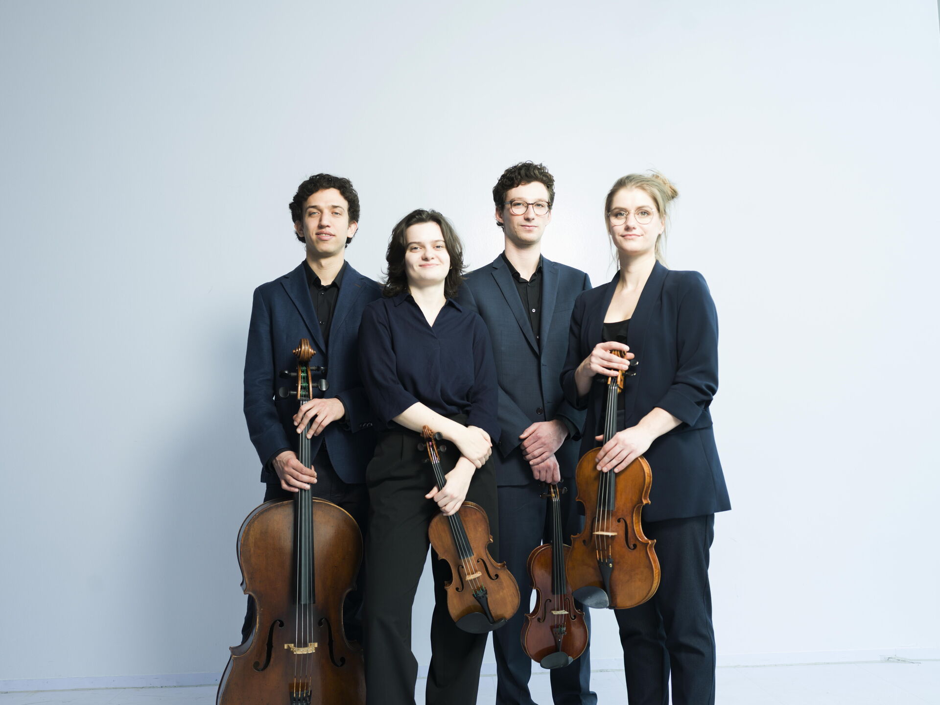 Klassiek strijkkwartet met twee violisten, een cellist en een altviolist, gekleed in zwarte outfits tegen een lichte achtergrond.