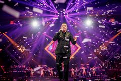 Marco Schuitmaker zingt op een podium terwijl confetti door paarse en gele lichtstralen dwarrelt.