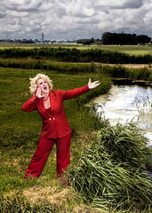 Karin Bloemen in een rood pak midden in een typisch Nederlands weiland.