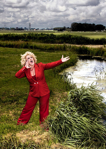 Karin Bloemen in een rood pak midden in een typisch Nederlands weiland.