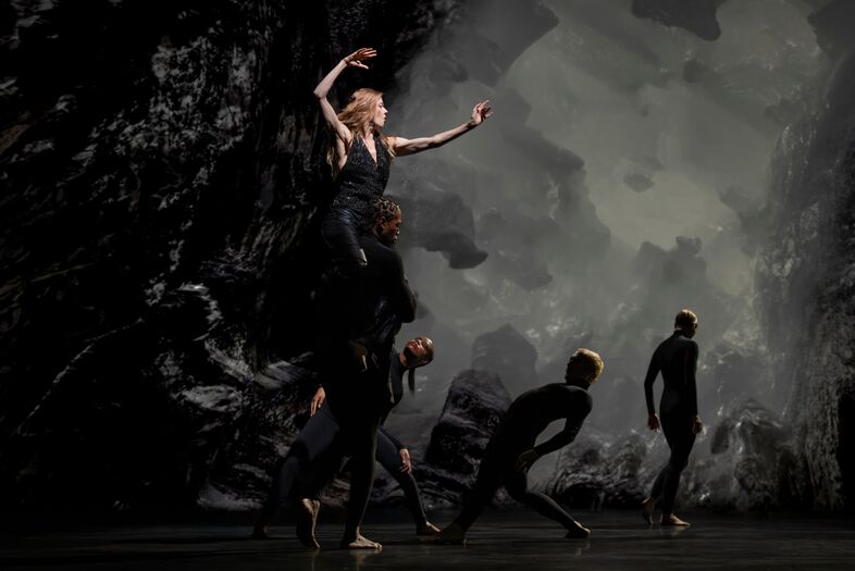 Dansgroep in dynamische pose op een abstracte achtergrond met grijstonen. Beweging en expressie staan centraal.