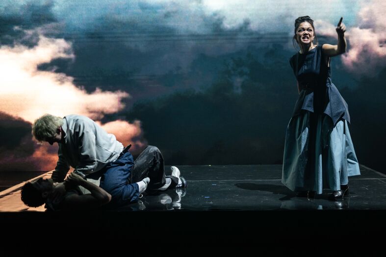 Theaterperformance met drie acteurs in een dramatische scène op een podium met een sfeervolle achtergrond.