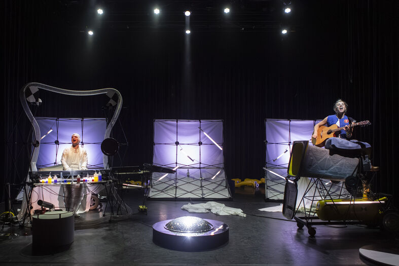 Een muzikale voorstelling met twee muzikanten, één op een gitaar en de andere achter een keyboard, op een sfeervol podium.