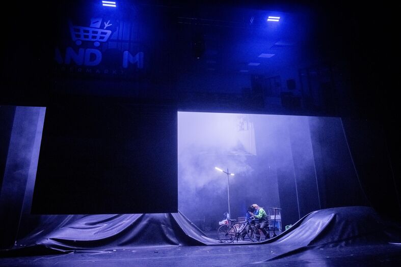 Theaterpodium met een blauwe belichting en een performer op een skateboard tussen glijbanen.