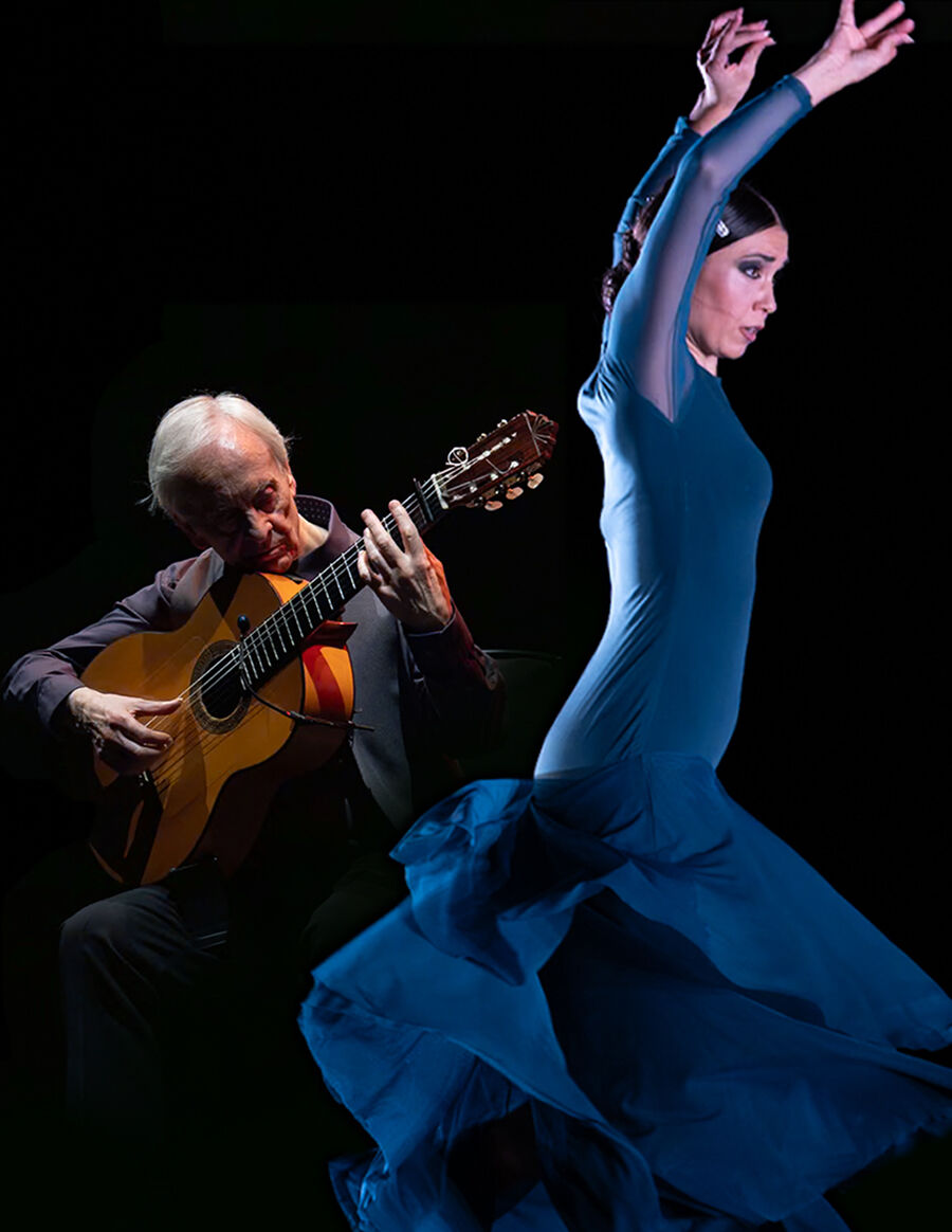 Een man met gitaar speelt terwijl een vrouw in een blauwe jurk danst, tegen een donkere achtergrond.