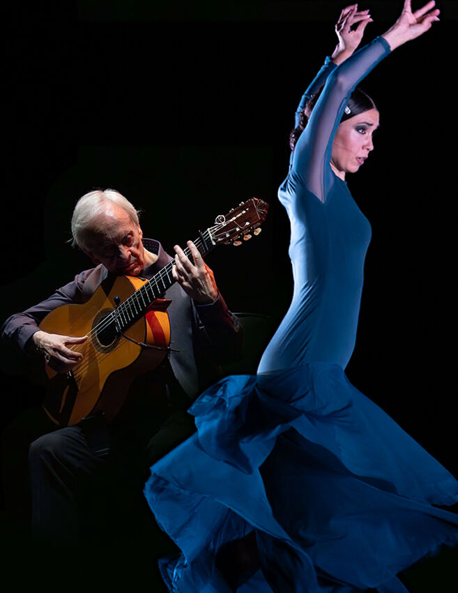 Een man met gitaar speelt terwijl een vrouw in een blauwe jurk danst, tegen een donkere achtergrond.