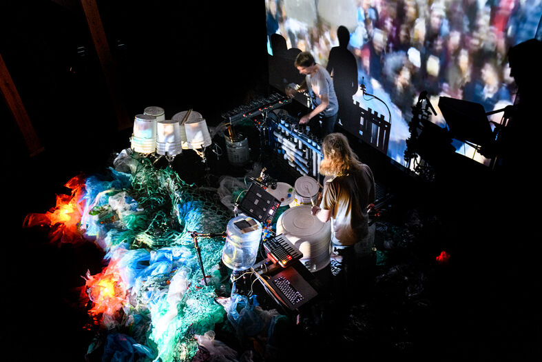 Een muzikant en DJ performen live op een podium met kleurrijke licht- en videoprojecties op de achtergrond.