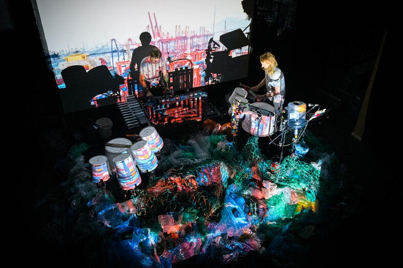 Een muzikant speelt op verschillende percussie-instrumenten met kleurrijke projecties op de achtergrond.